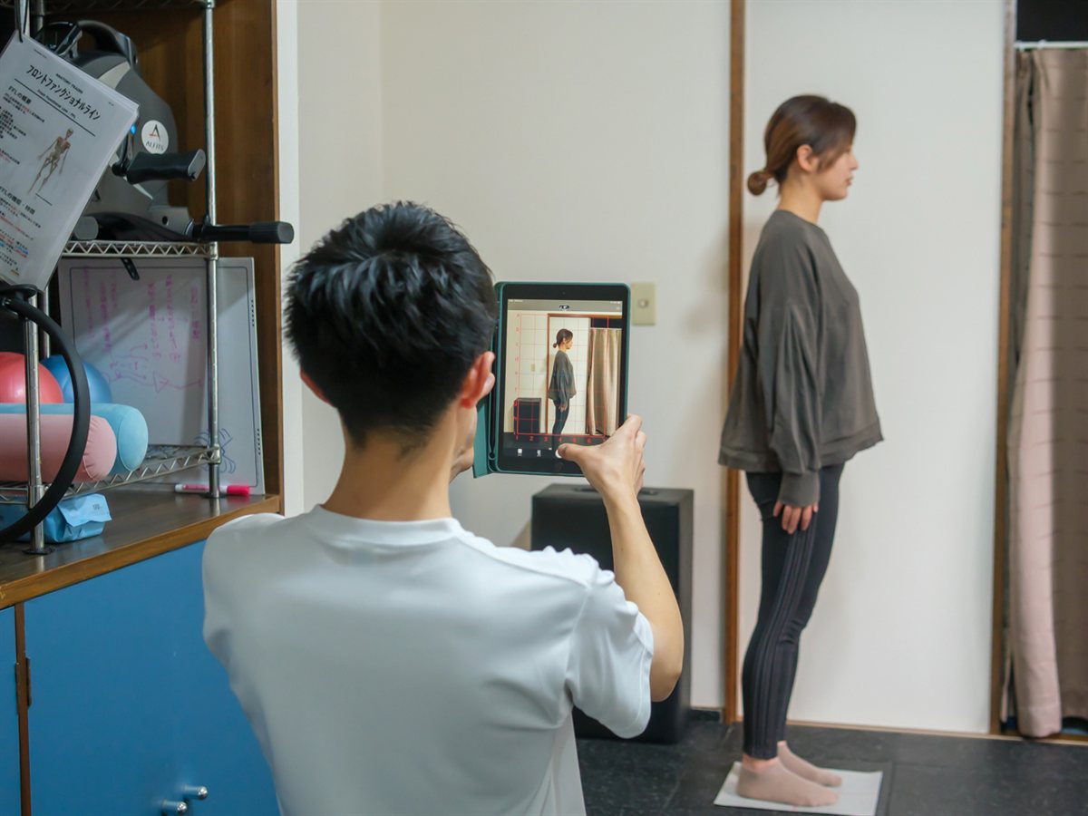 理学療法士がタブレットで姿勢を撮影して評価している場面